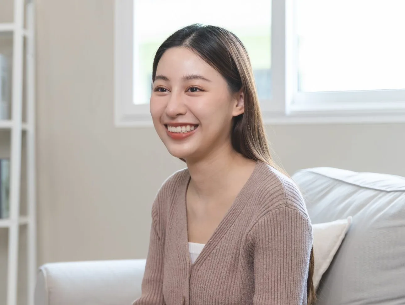 Woman smiling while seated on bed in bright, modern bedroom