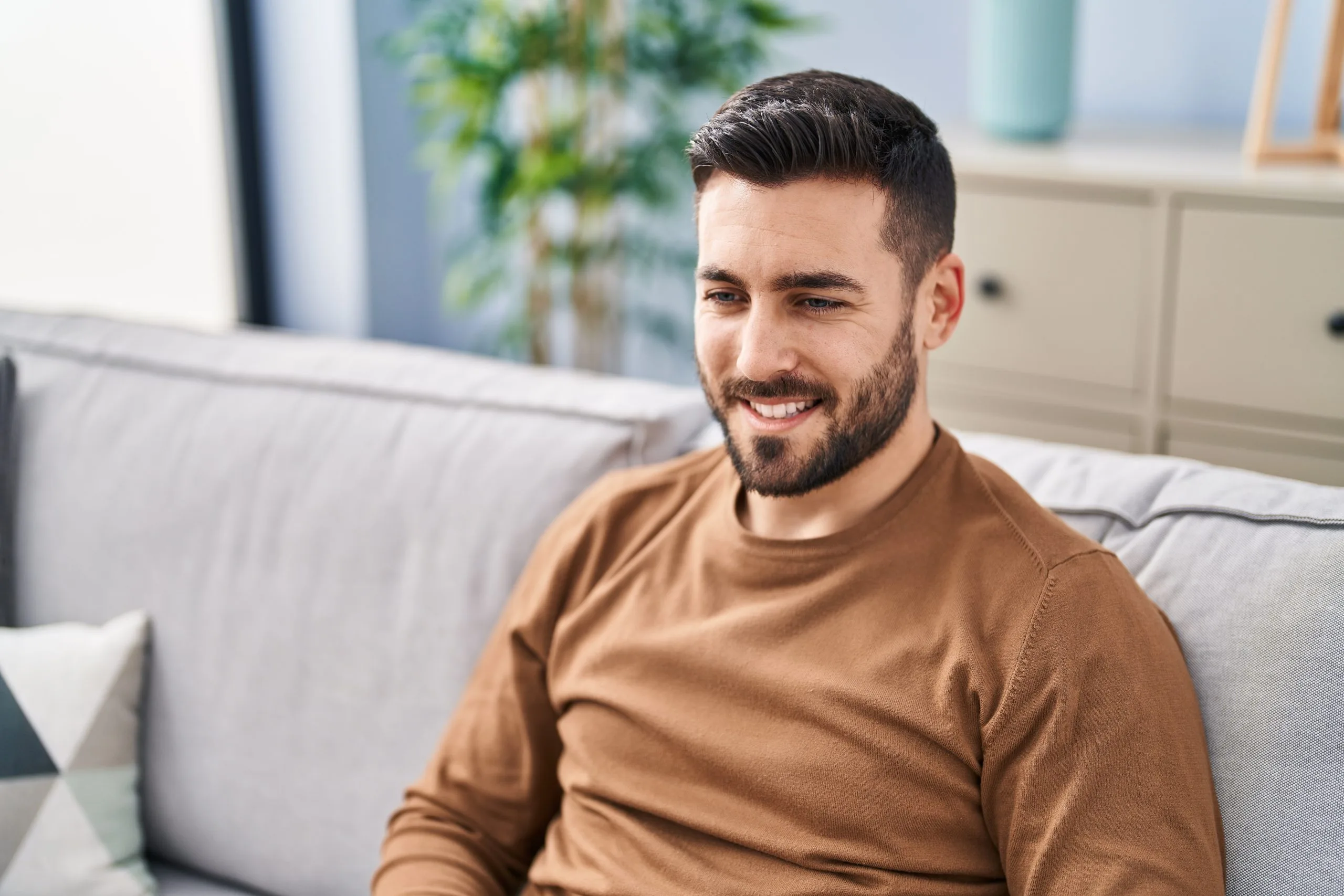 Smiling man sitting on couch in bright home interior with plants and furniture