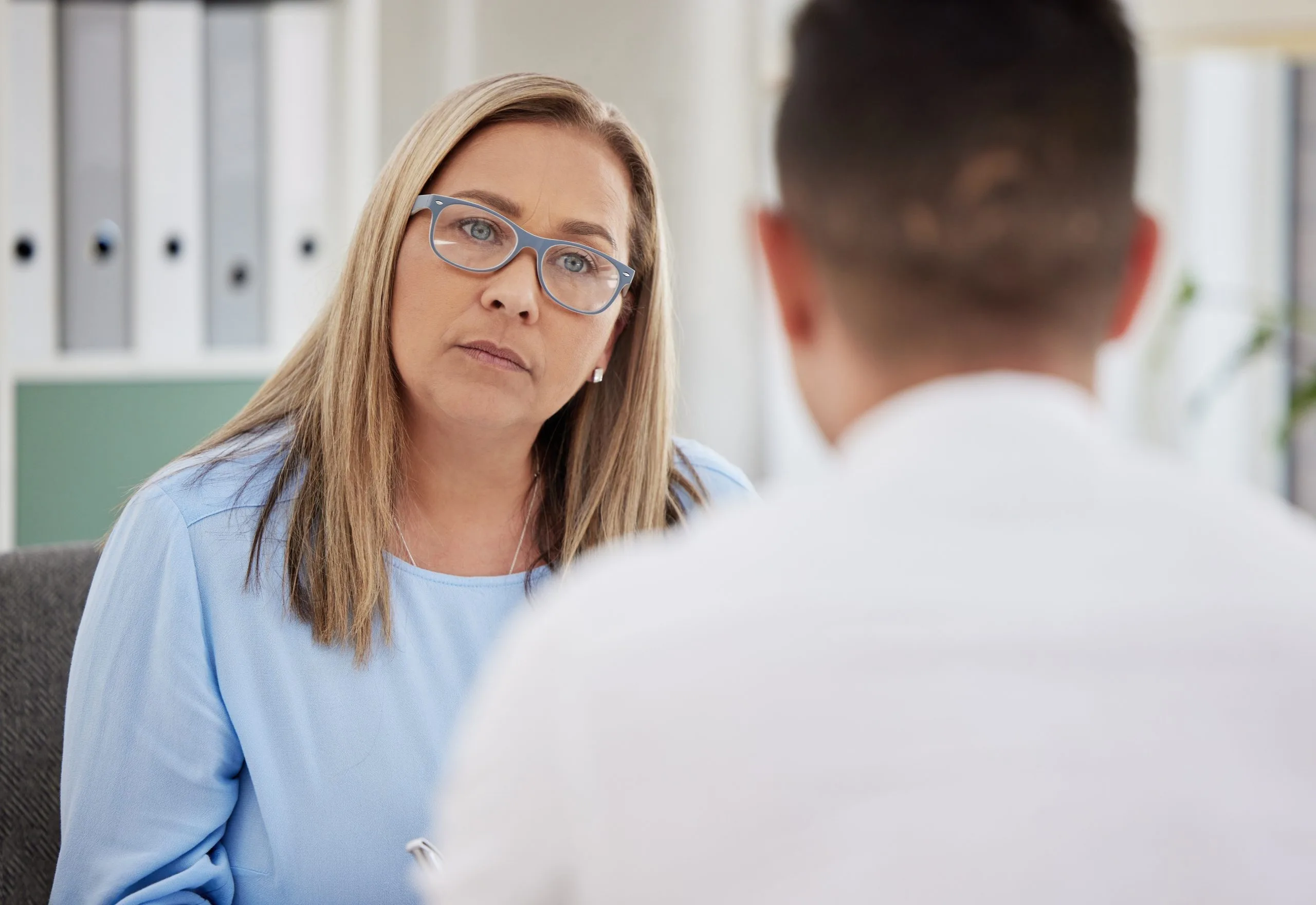 Therapist in blue shirt and glasses listening to patient during counseling session