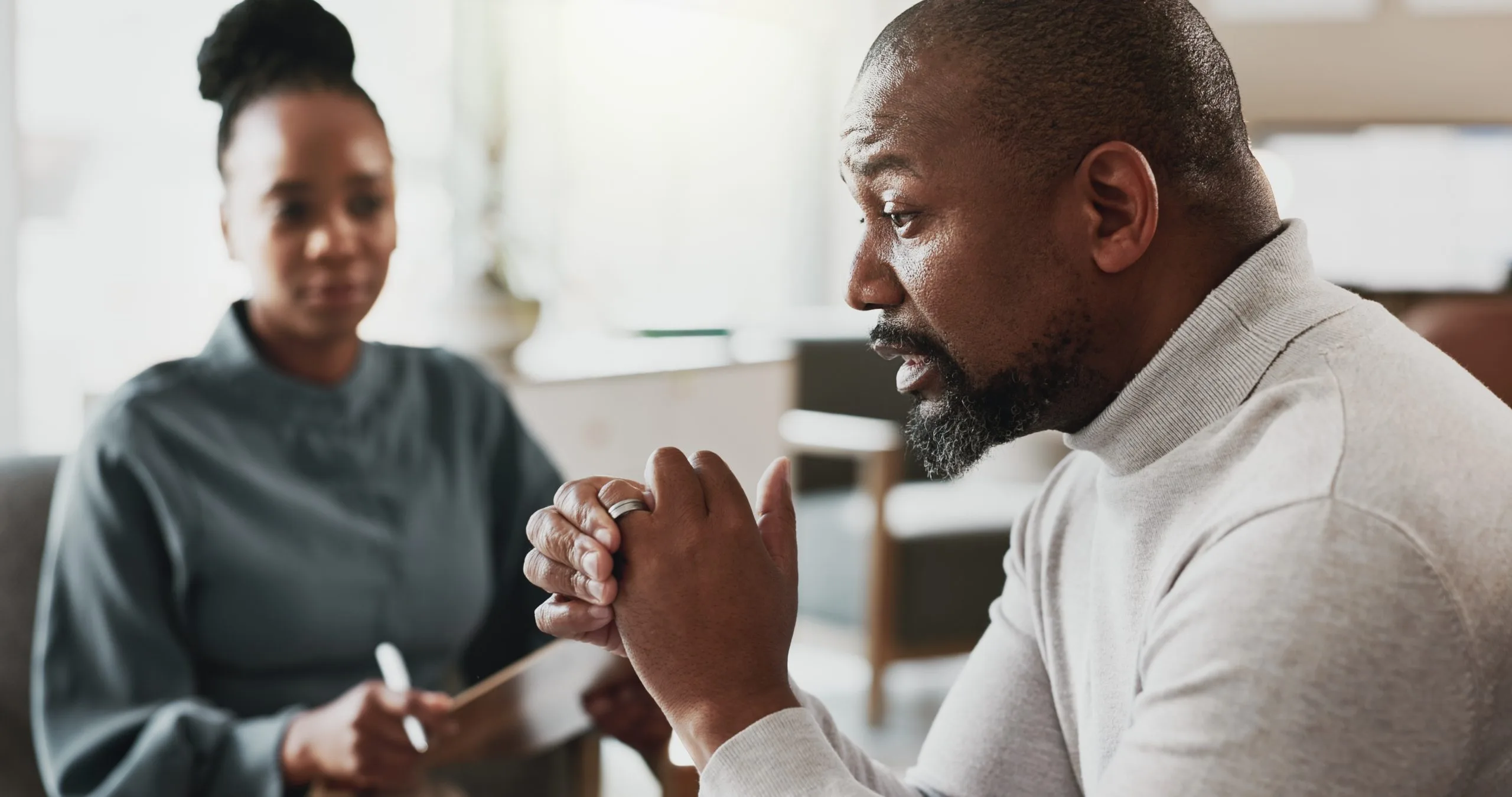 Man in therapy session discussing concerns with female clinician taking notes