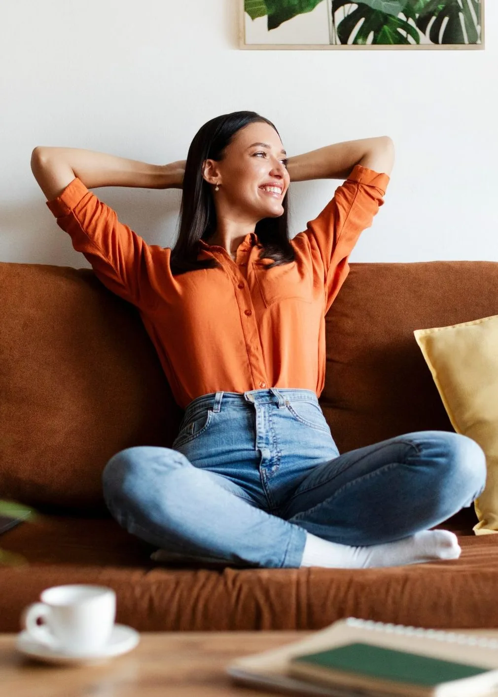 Woman relaxing on couch with hands behind head, smiling contentedly