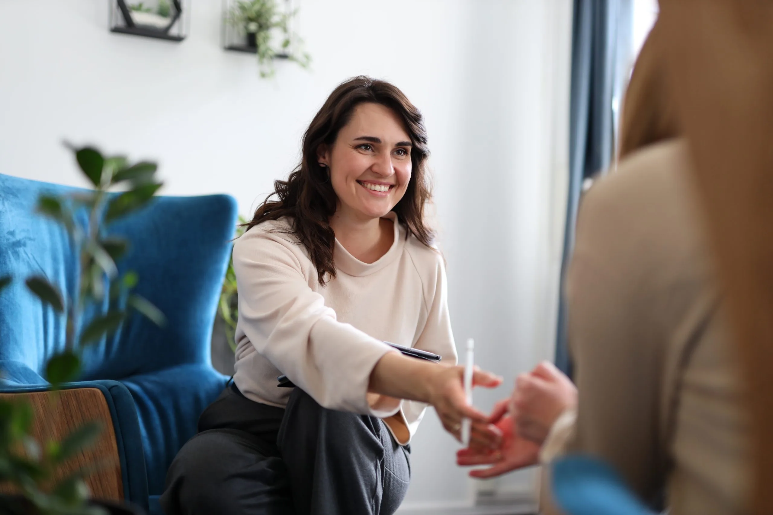 Therapist smiling while engaging with a patient during a counseling session in a bright office with plants