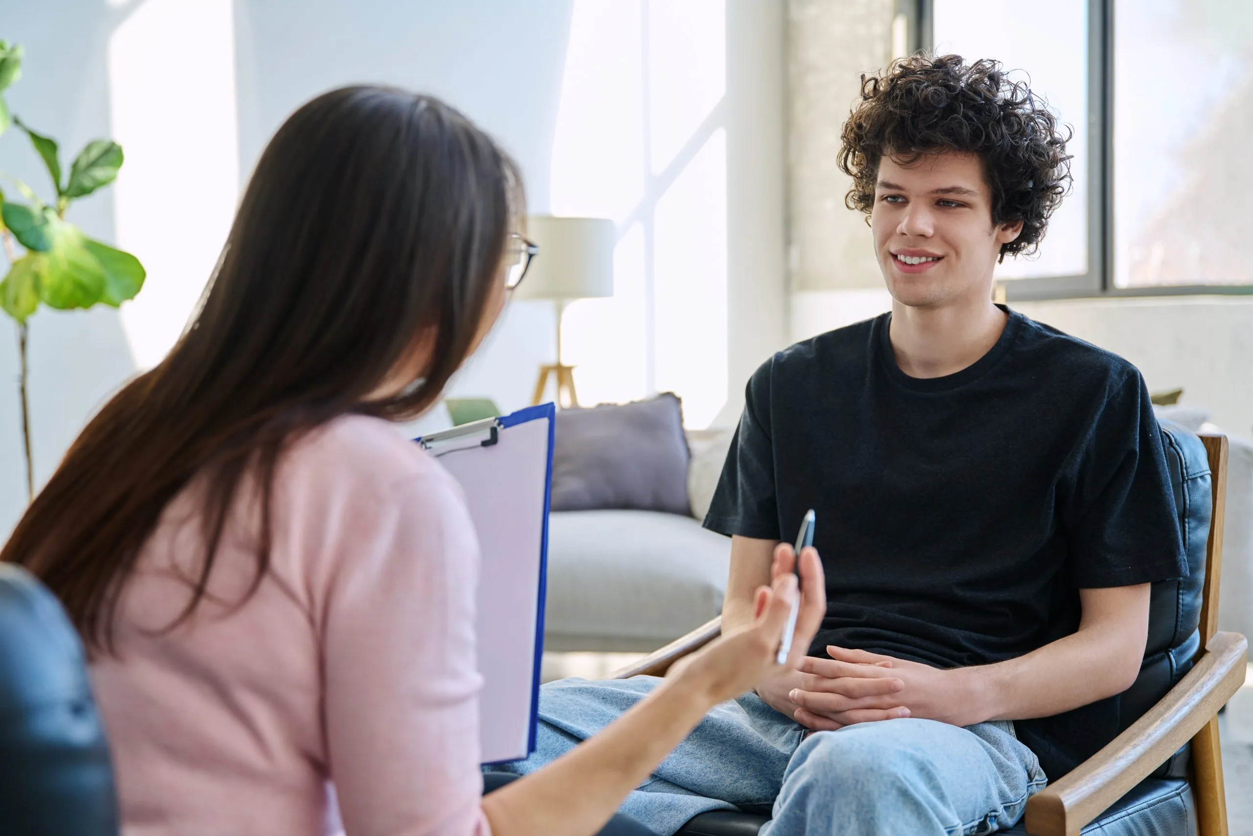 Young man in therapy session speaking with female clinician in bright office