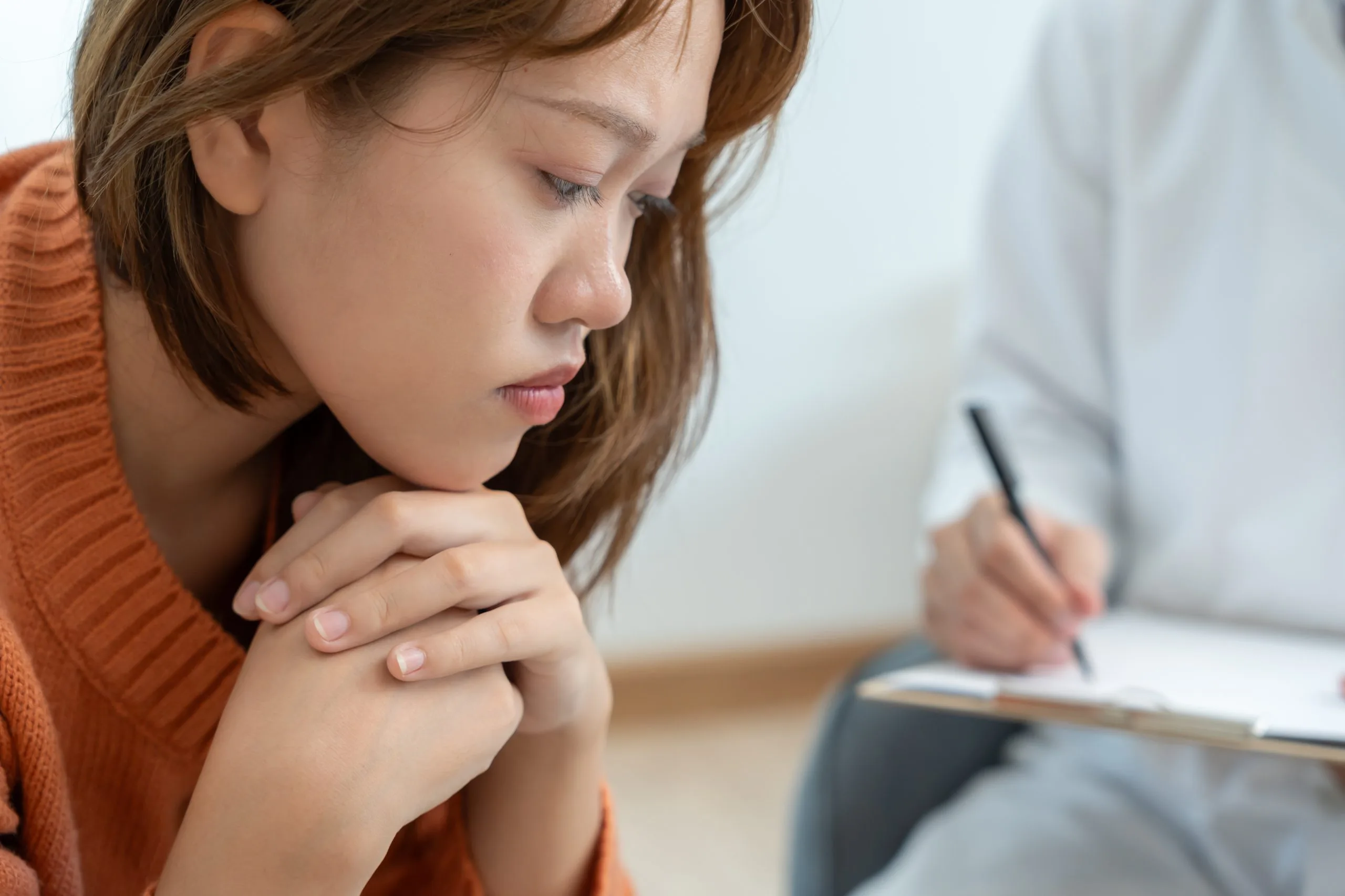 Anxious girl with hand on shoulder while clinician writes notes on clipboard
