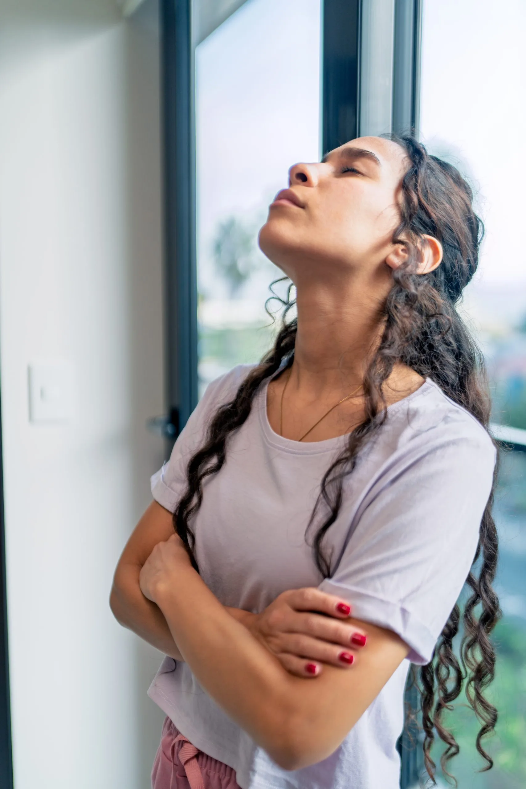 Woman with braided hair gazing upward by a window with a landscape view