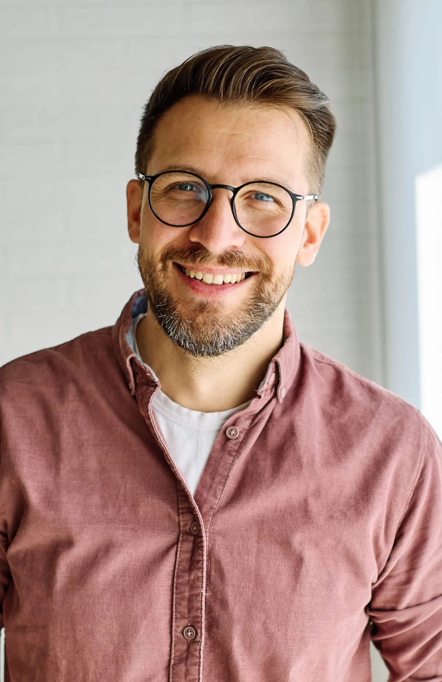 Smiling man wearing glasses and a pink button-up shirt against a white background