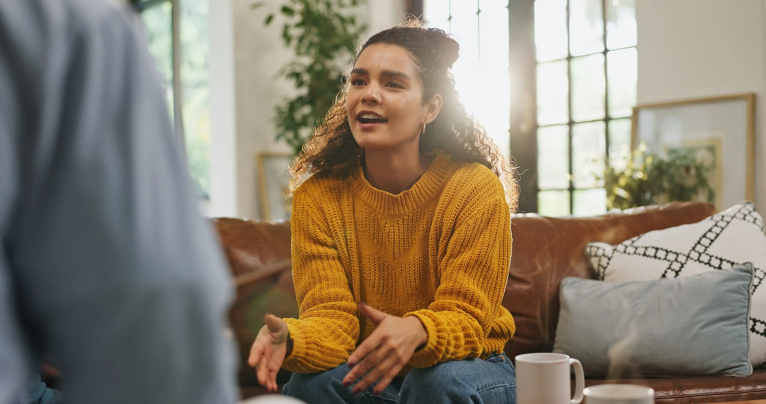 Woman in yellow sweater speaking with a therapist on a brown couch in a sunlit room