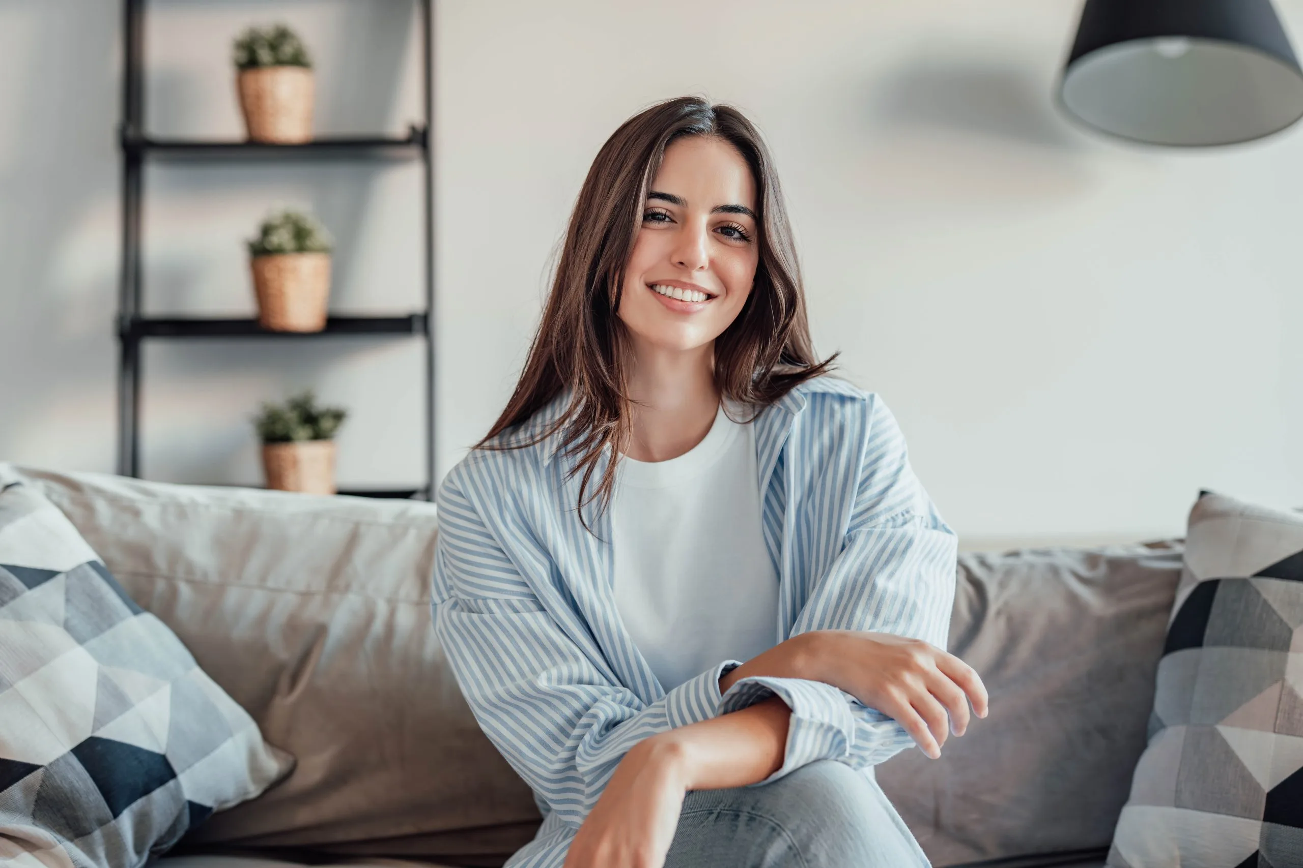 Woman smiling while sitting on couch with potted plants and pendant lamp in background