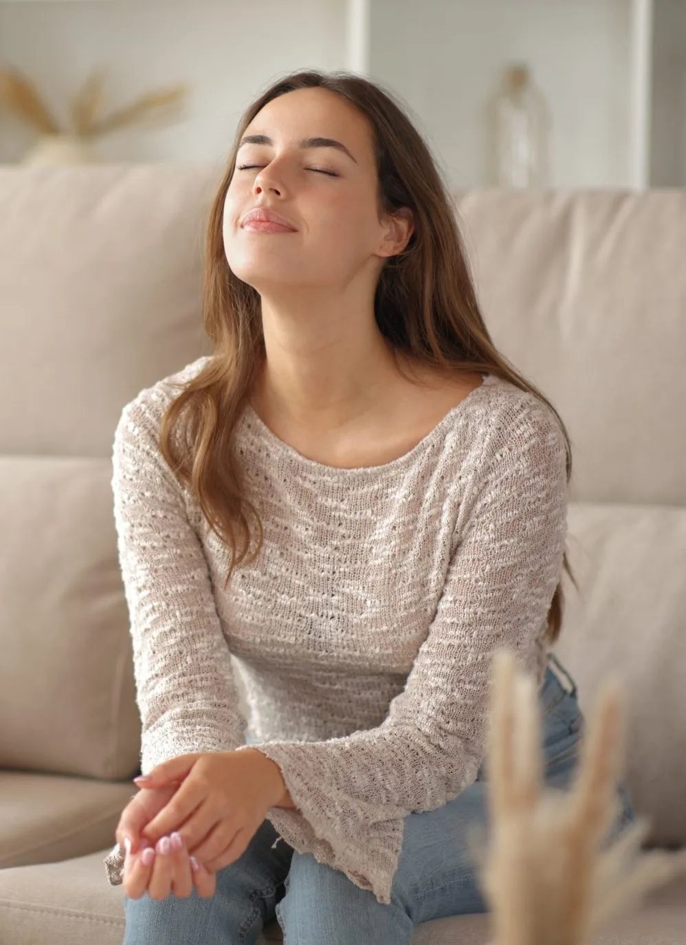 Woman with eyes closed sitting on couch, appearing calm and peaceful