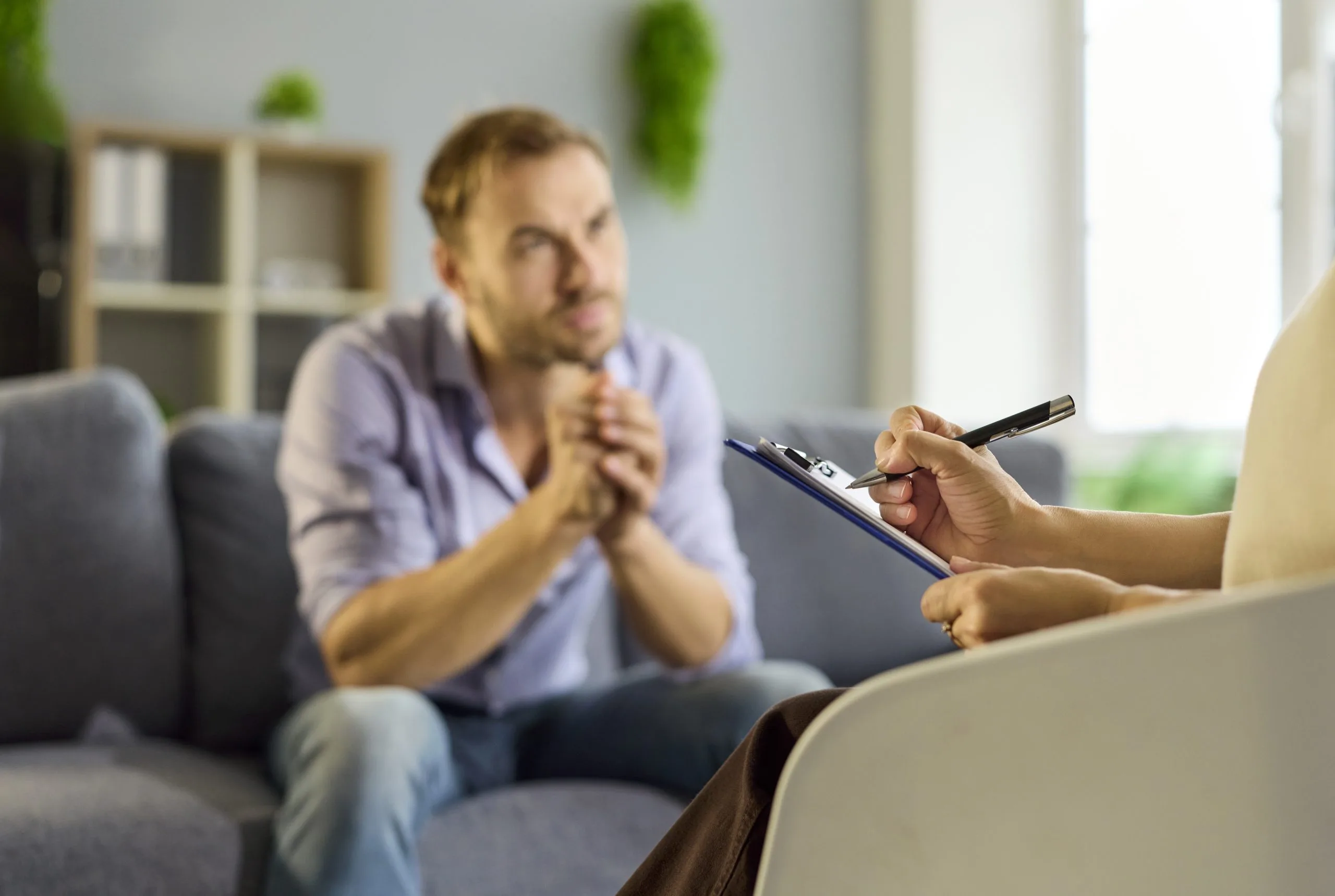 Therapist taking notes during therapy session with male patient on gray couch