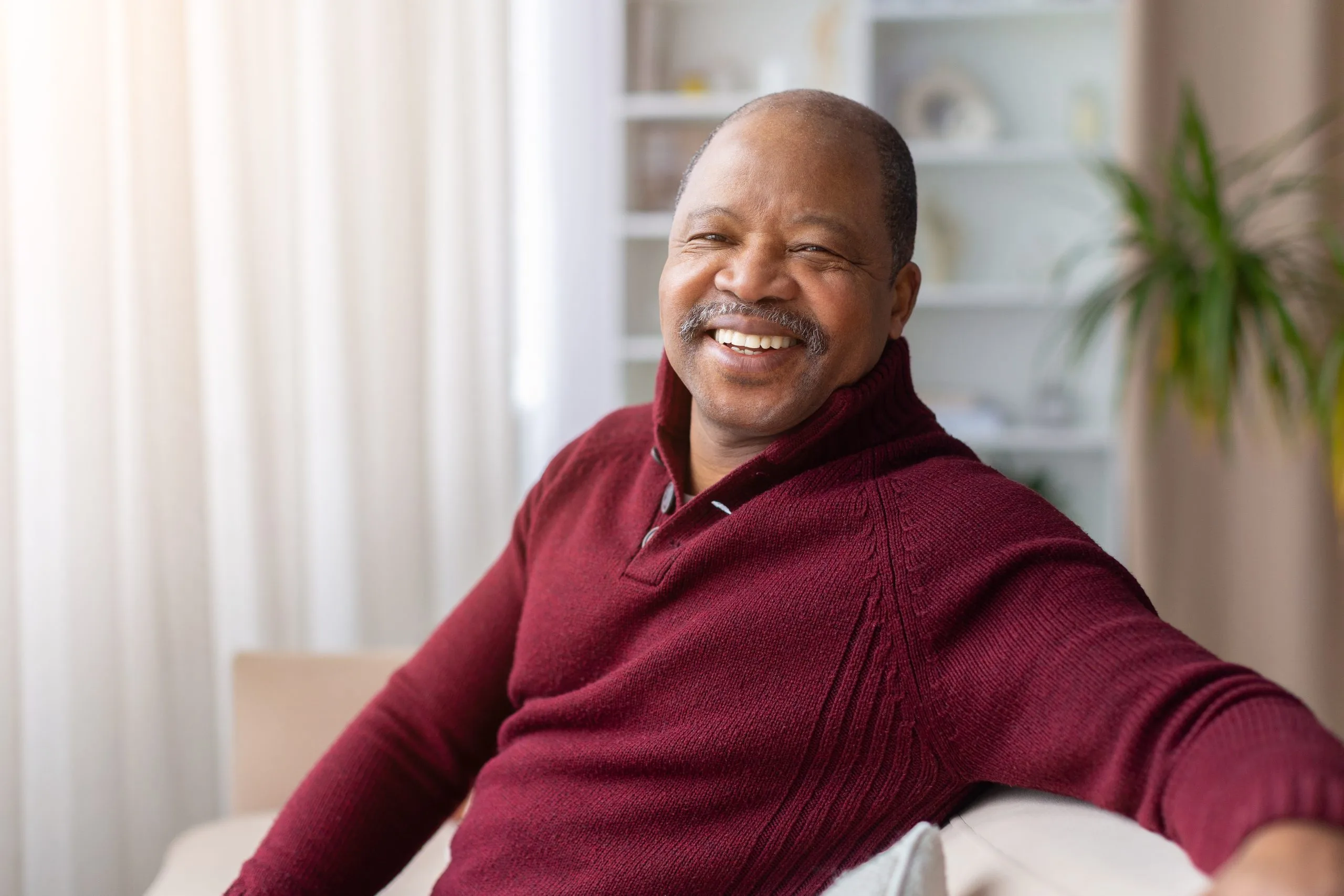 Man in maroon sweater smiling at camera in bright indoor setting