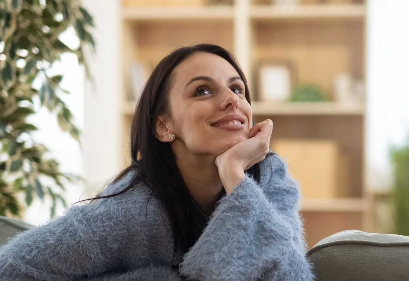 Woman resting chin on hand, looking thoughtfully upward in modern living room