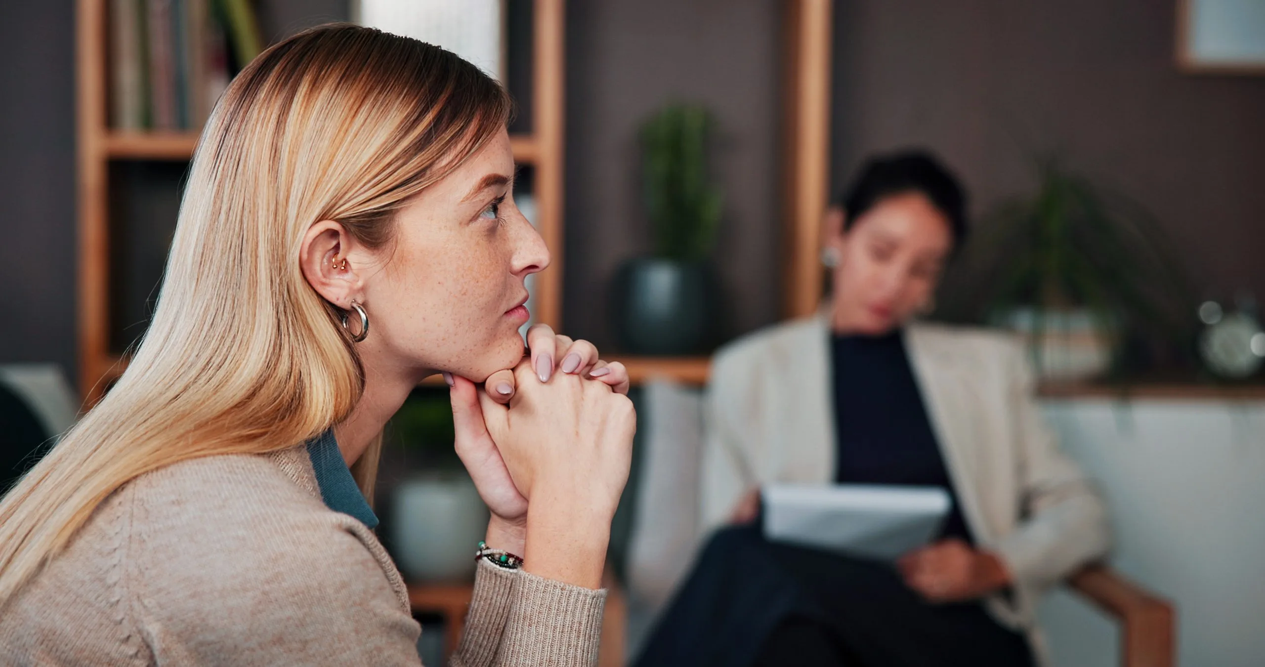 Patient in profile looking thoughtful during a therapy session while therapist takes notes in background