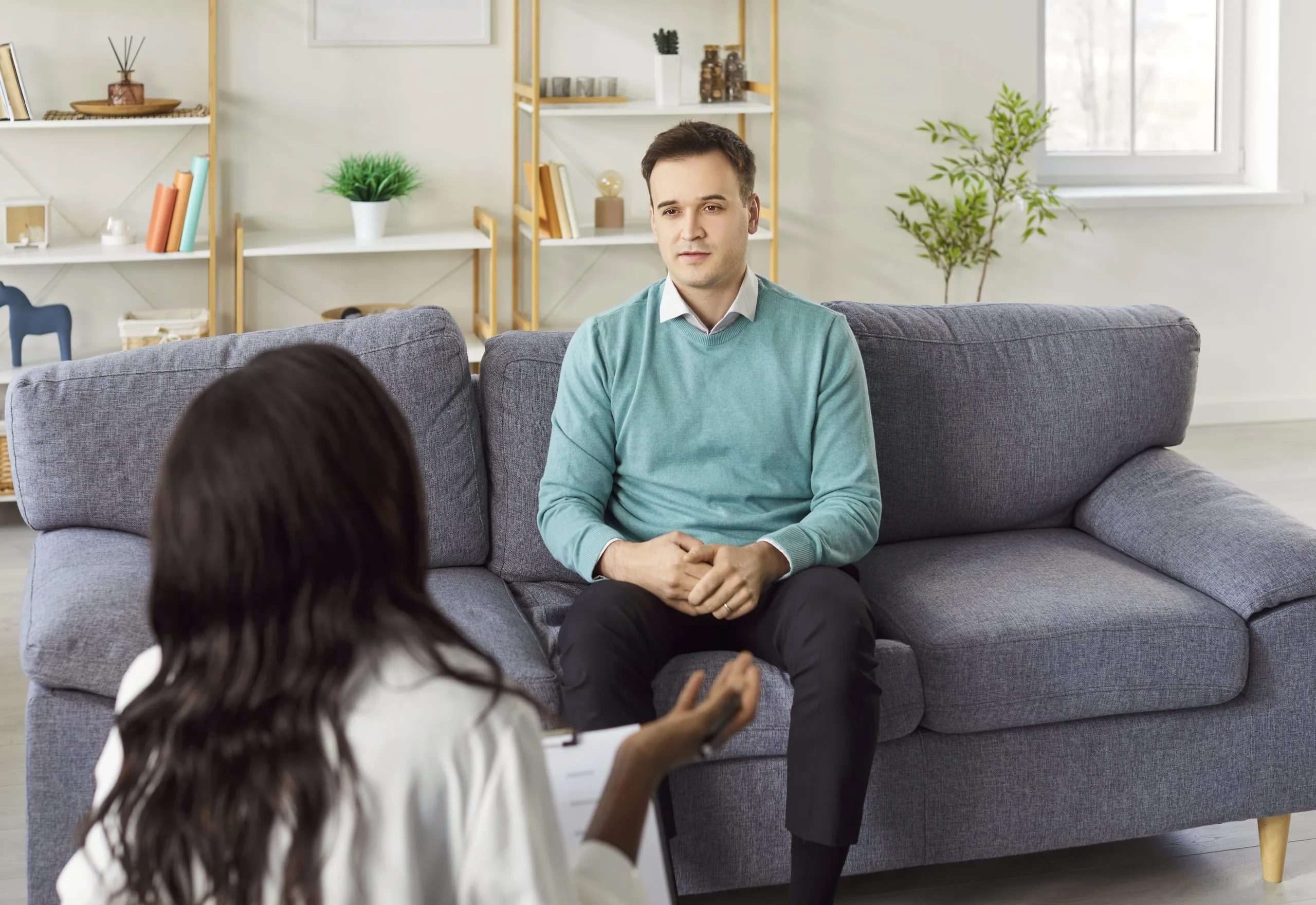 Therapist listening to a patient sitting across from him on a gray couch in a modern office