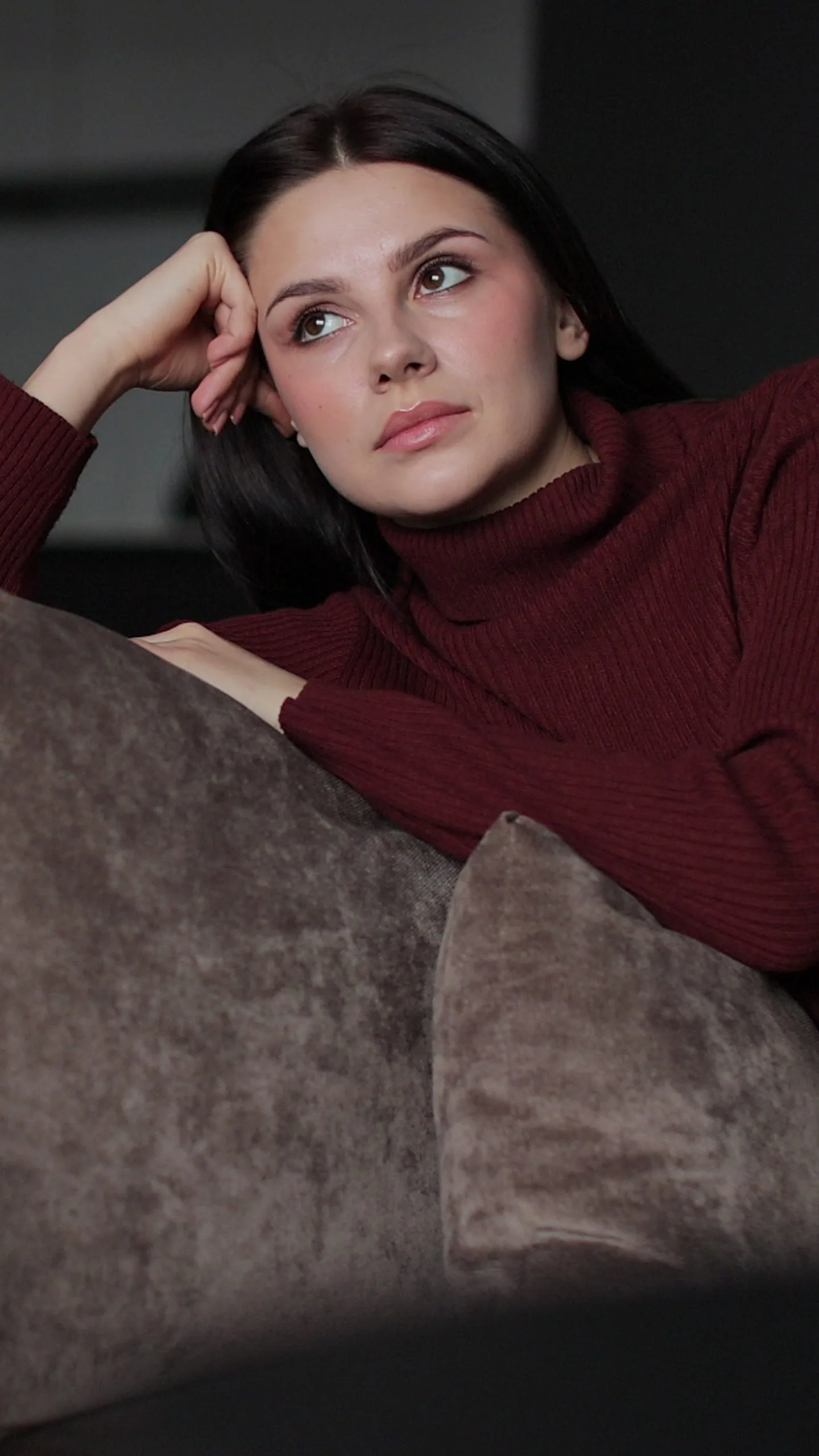 Woman in burgundy turtleneck resting head on hand against gray background