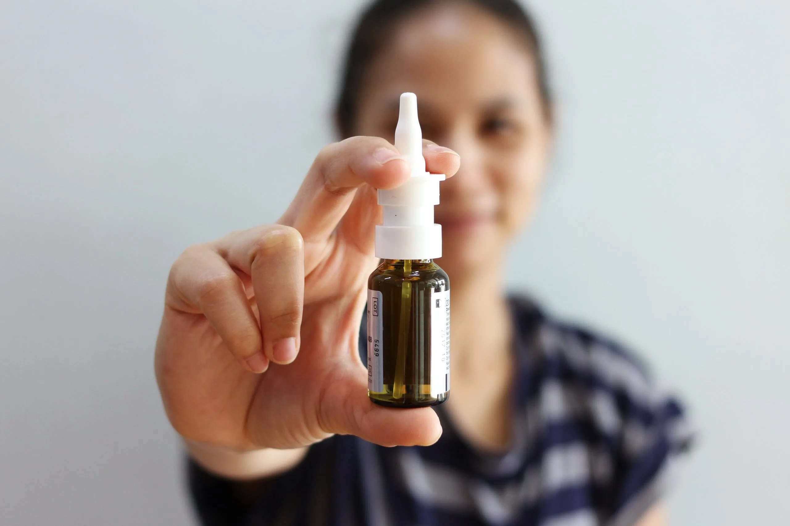 Woman holding a nasal spray bottle toward the camera with a blurred face in background