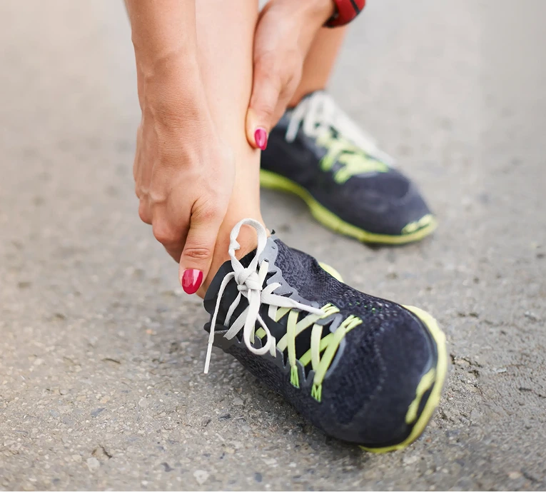 Runner holding ankle while wearing black and neon athletic shoes on pavement