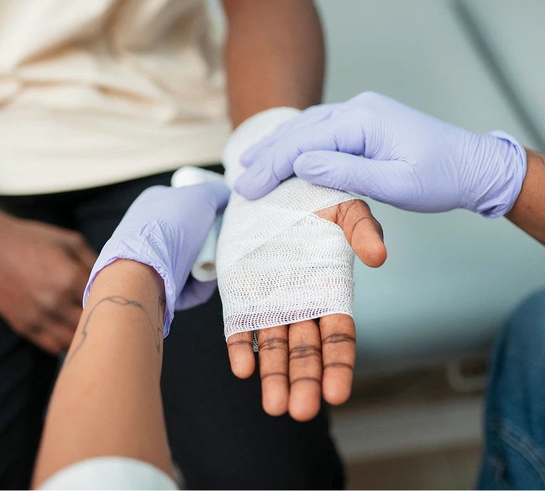 Healthcare provider in purple gloves examining a patient's hand wrapped in white bandage