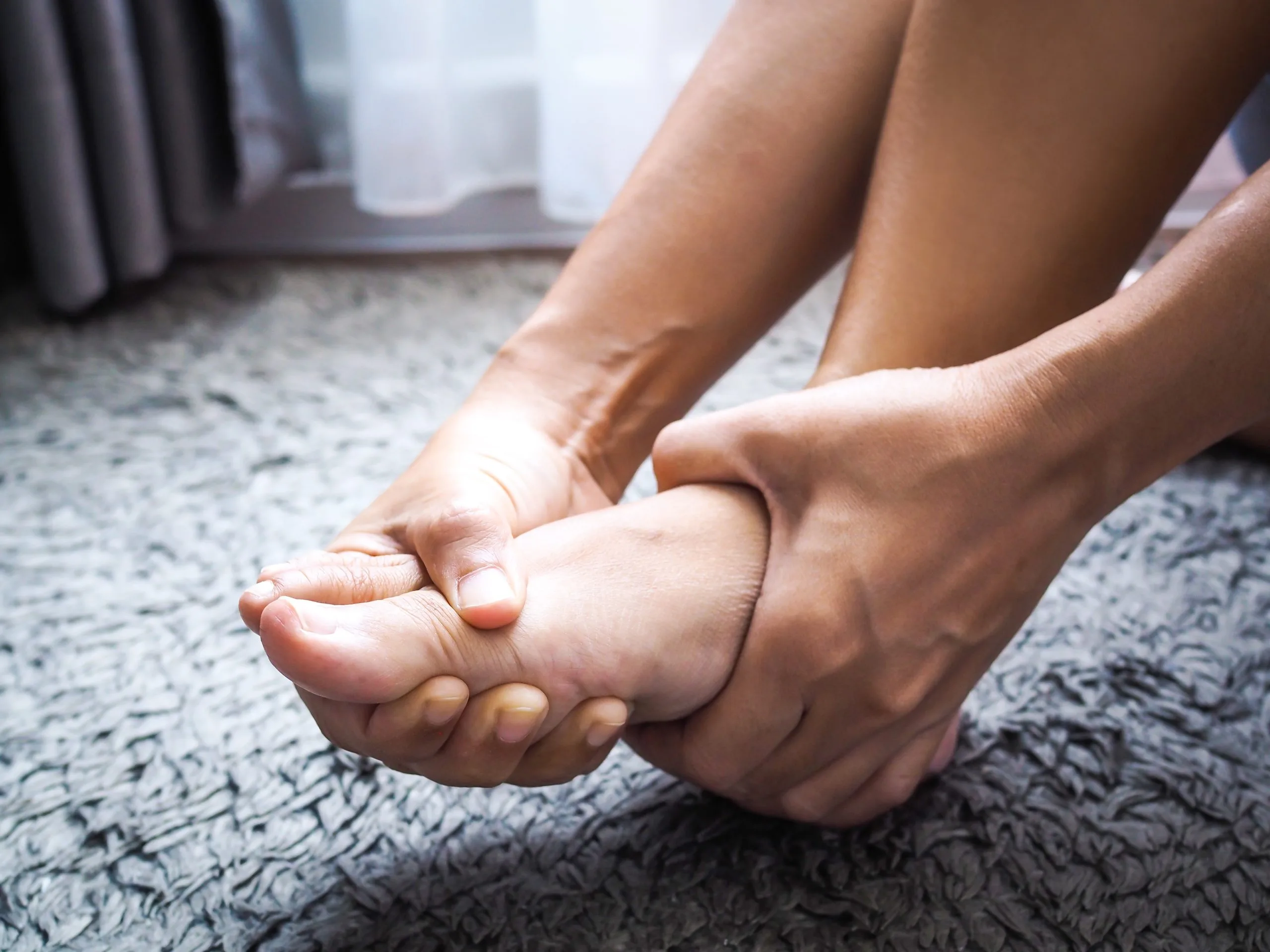 Hands massaging foot on textured carpet surface
