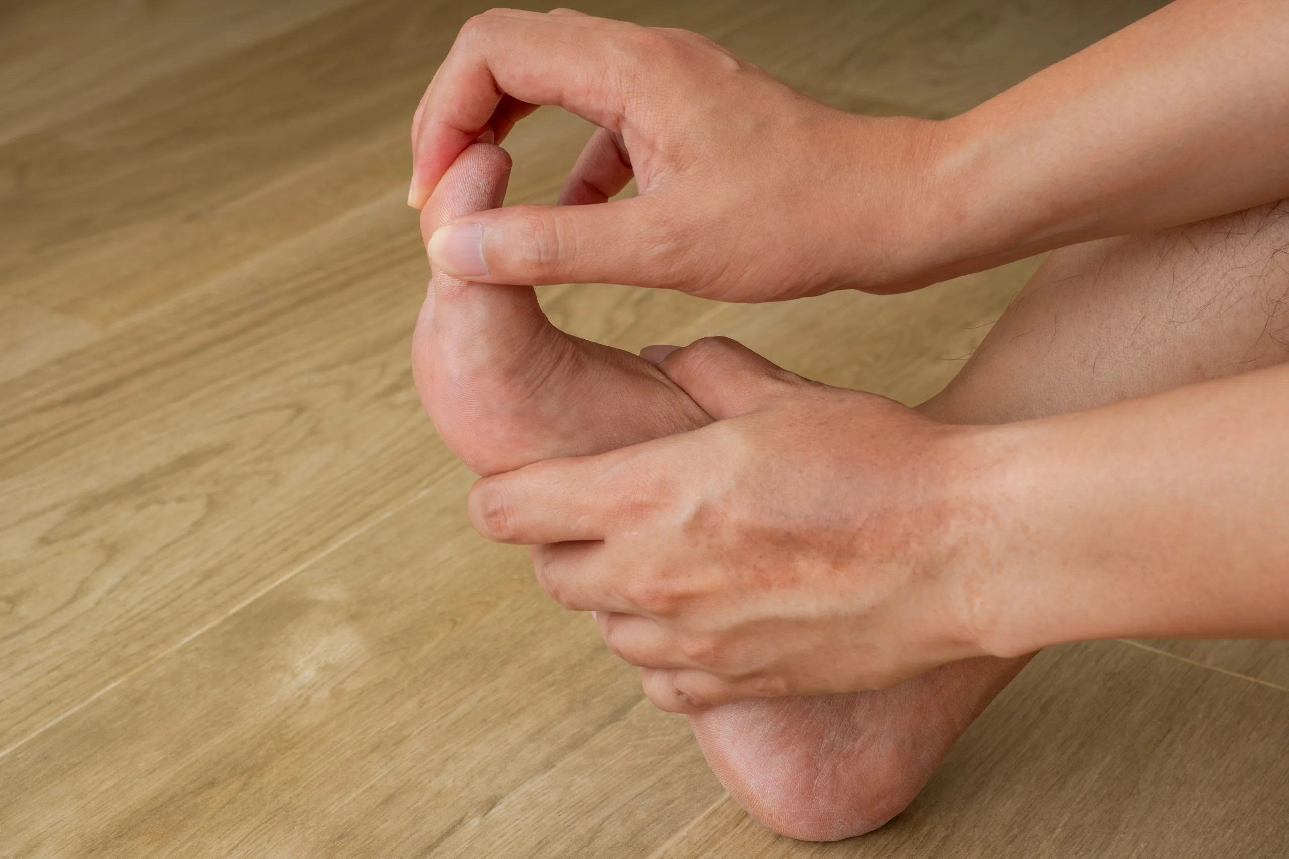 Hands palpating a patient's foot and ankle on wooden floor