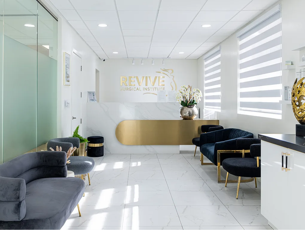 Revive Surgical Institute reception area with gold desk, black chairs, and gold logo on white wall
