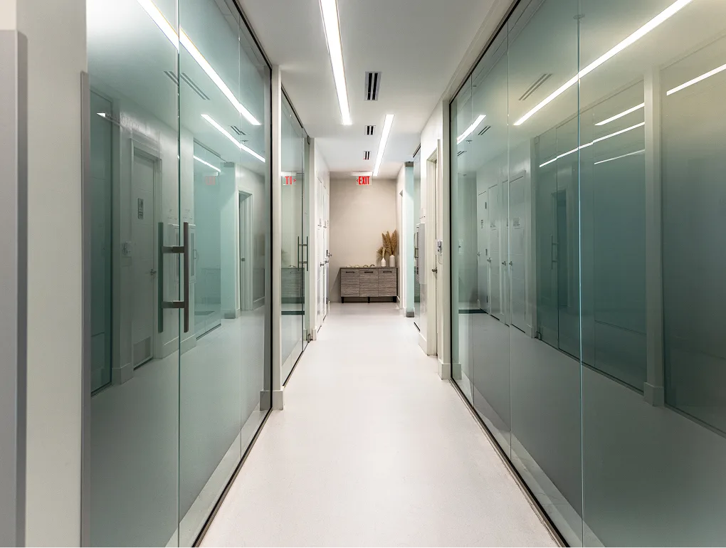 Modern surgical hallway with frosted glass treatment rooms and bright linear ceiling lights