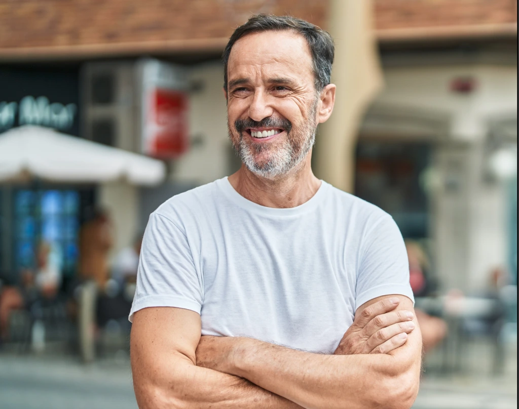 Middle-aged man with gray beard and crossed arms smiling at outdoor street location