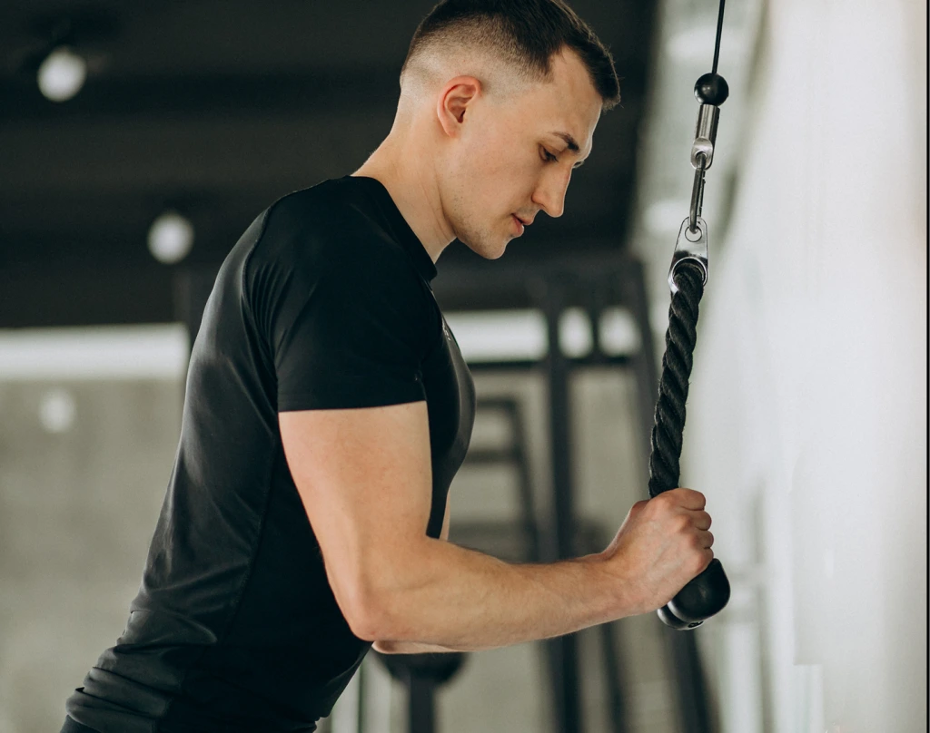 Young man in black t-shirt gripping a hanging rope in a gym setting