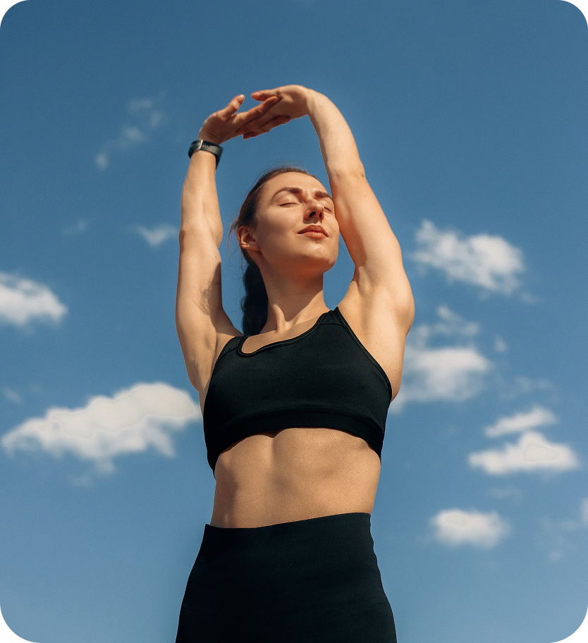 Woman stretching arms overhead against clear blue sky with white clouds
