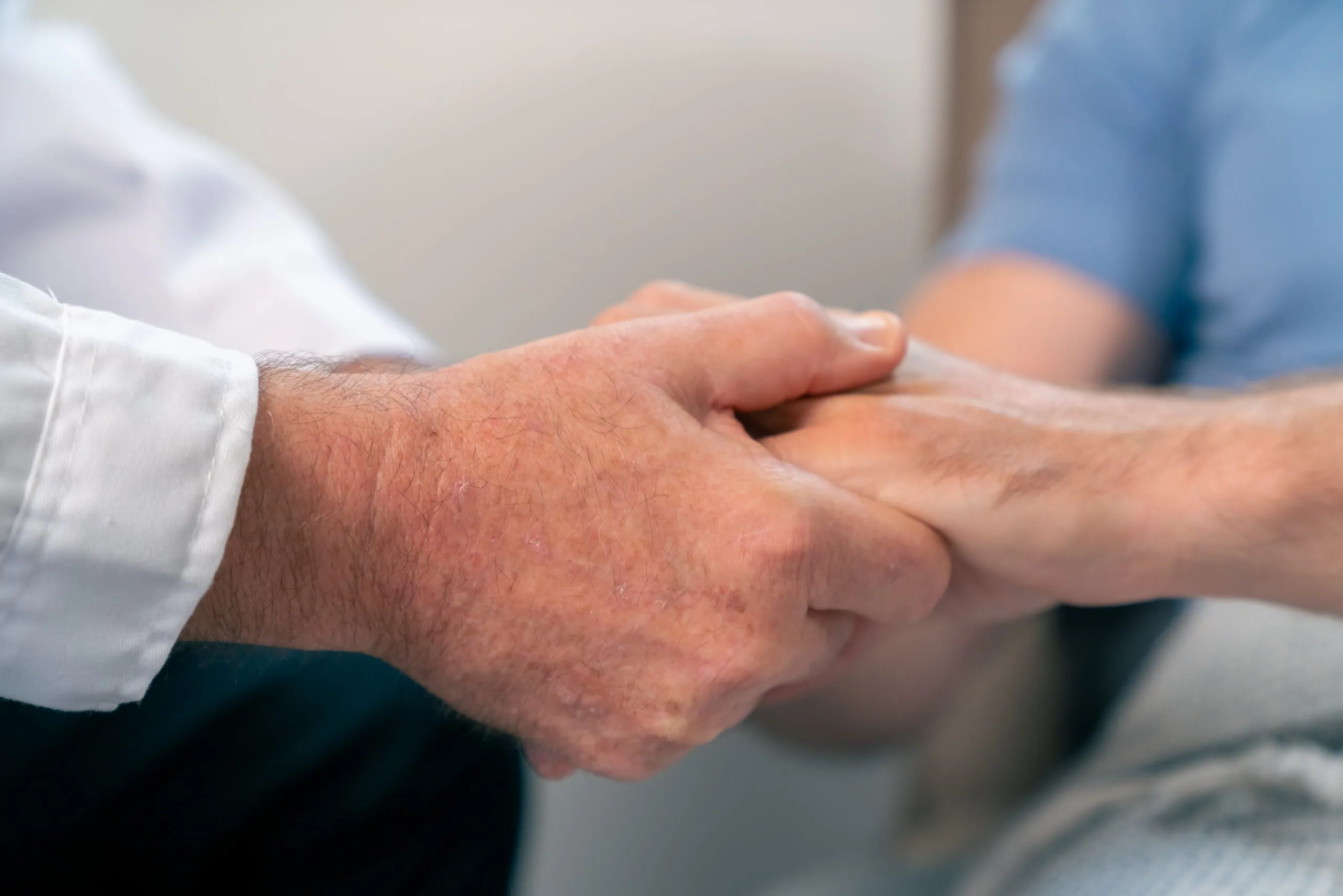 Healthcare provider in white coat shaking hands with patient in blue shirt
