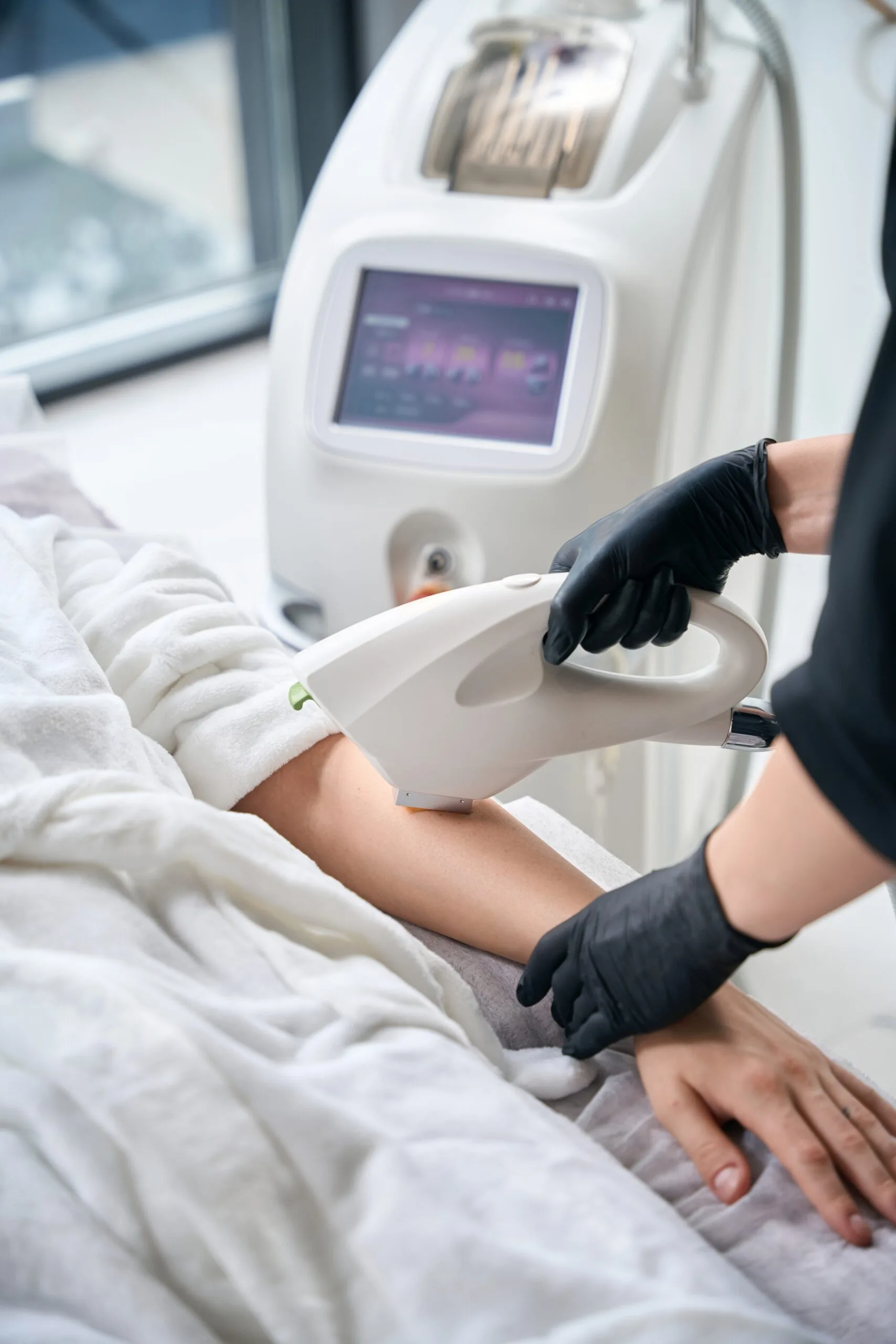Practitioner operating laser machine with display screen while treating patient's arm