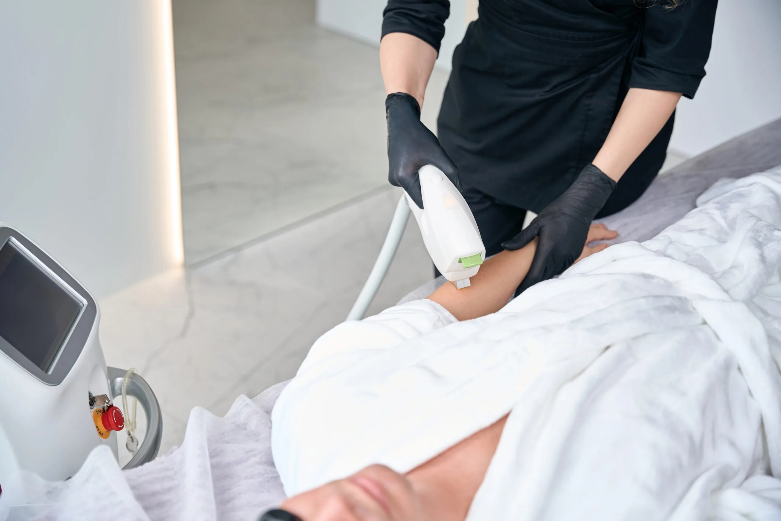 Practitioner in black gloves using laser applicator on patient's leg during procedure
