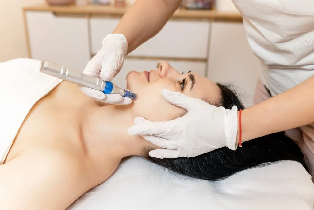 Aesthetician in white gloves performing microneedling treatment on patient's face with handheld device