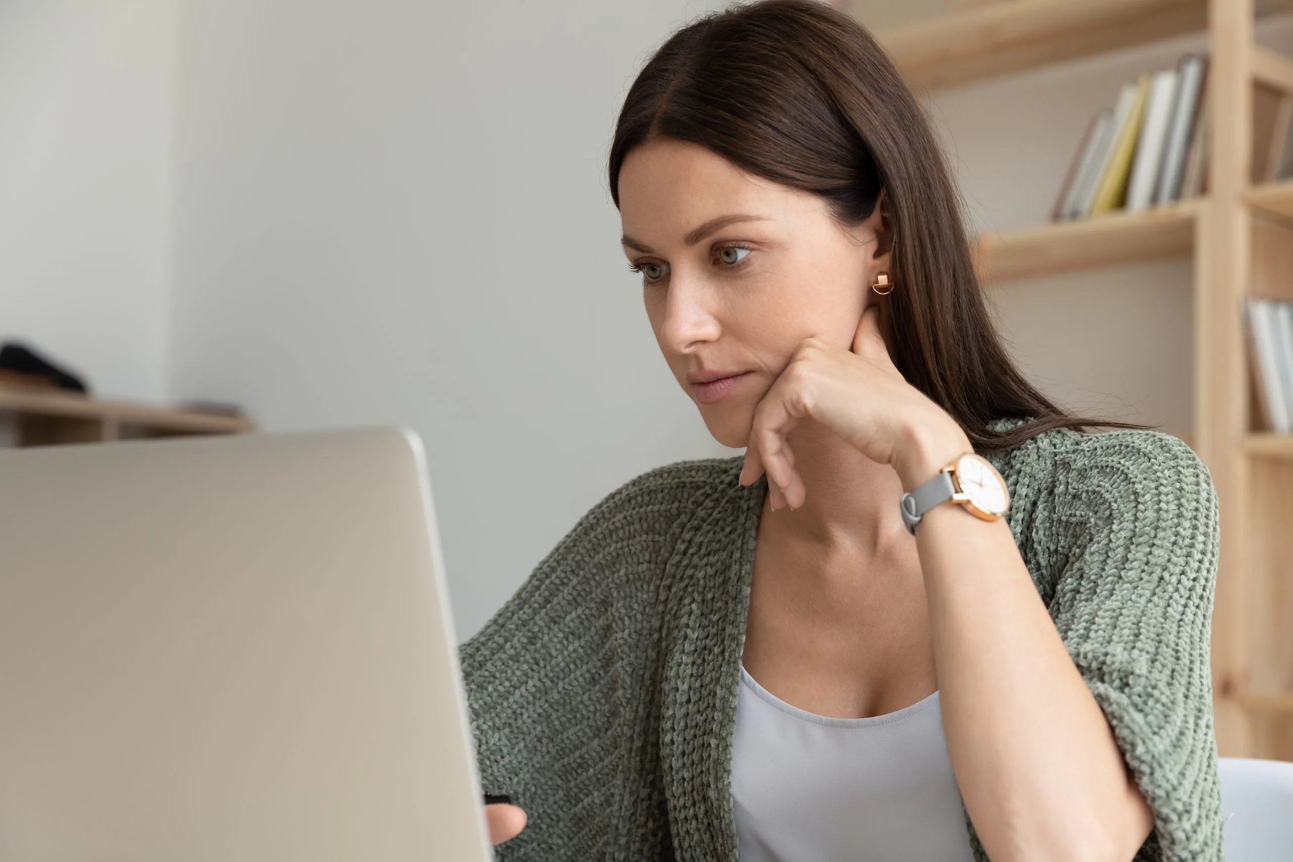 Woman at laptop looking thoughtful while considering cosmetic surgery options
