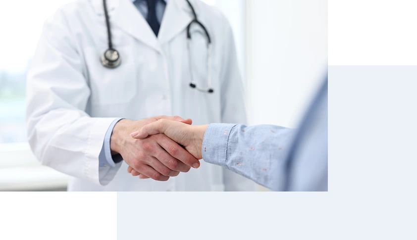 Healthcare provider in white coat and stethoscope shaking hands with patient