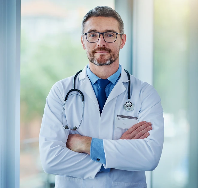 Male doctor wearing glasses and stethoscope, arms crossed, in white coat and blue shirt