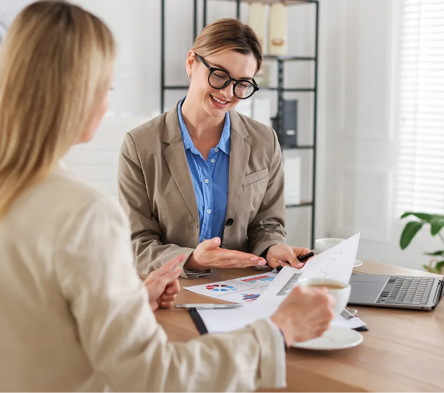 Business consultant in glasses and blazer reviewing charts with a client at a desk