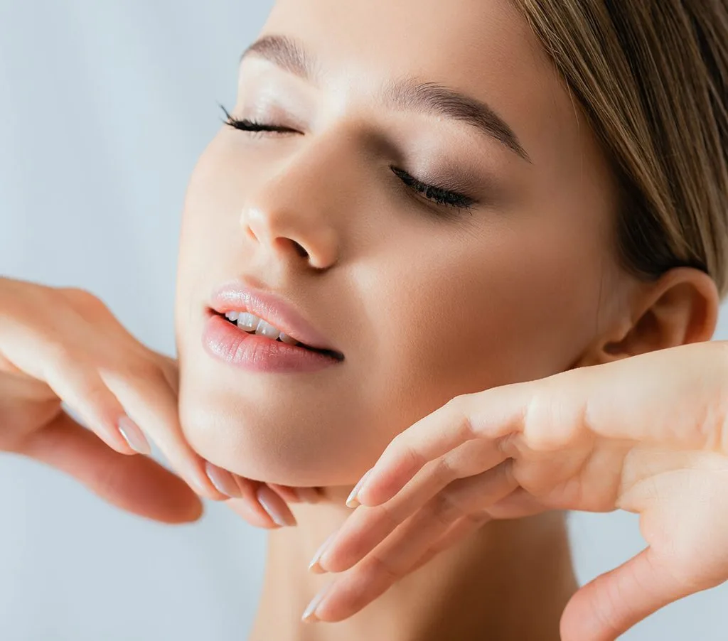 Woman with eyes closed touching her smooth face and neck