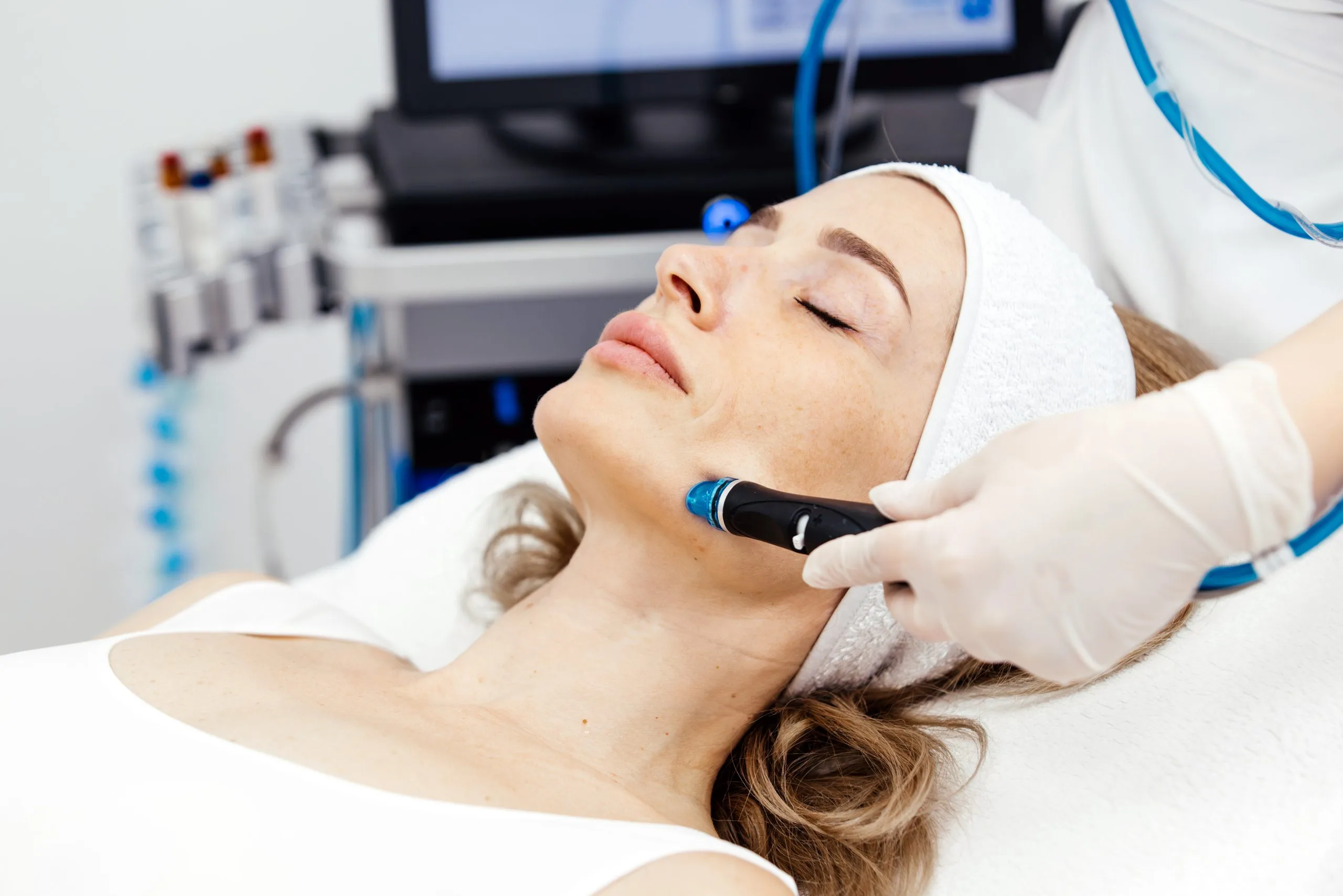 Practitioner using handheld ultrasound device on woman's cheek during facial treatment