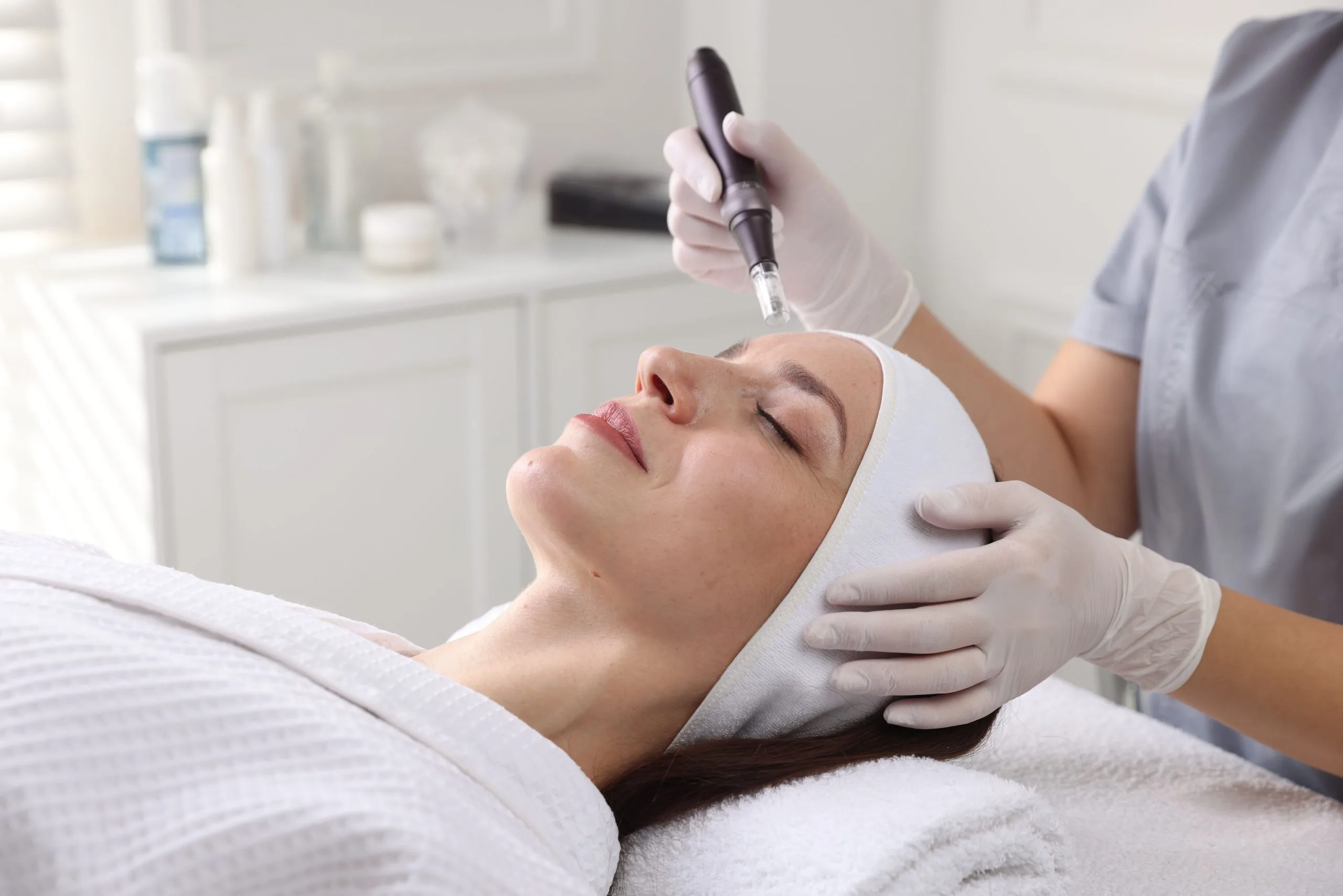 Practitioner performing microneedling procedure on woman's face in beauty salon setting