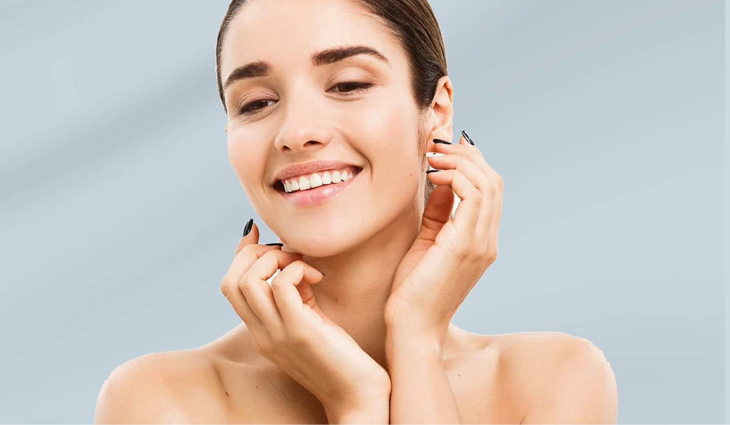 Woman with clear skin smiling and touching her face against a light blue background