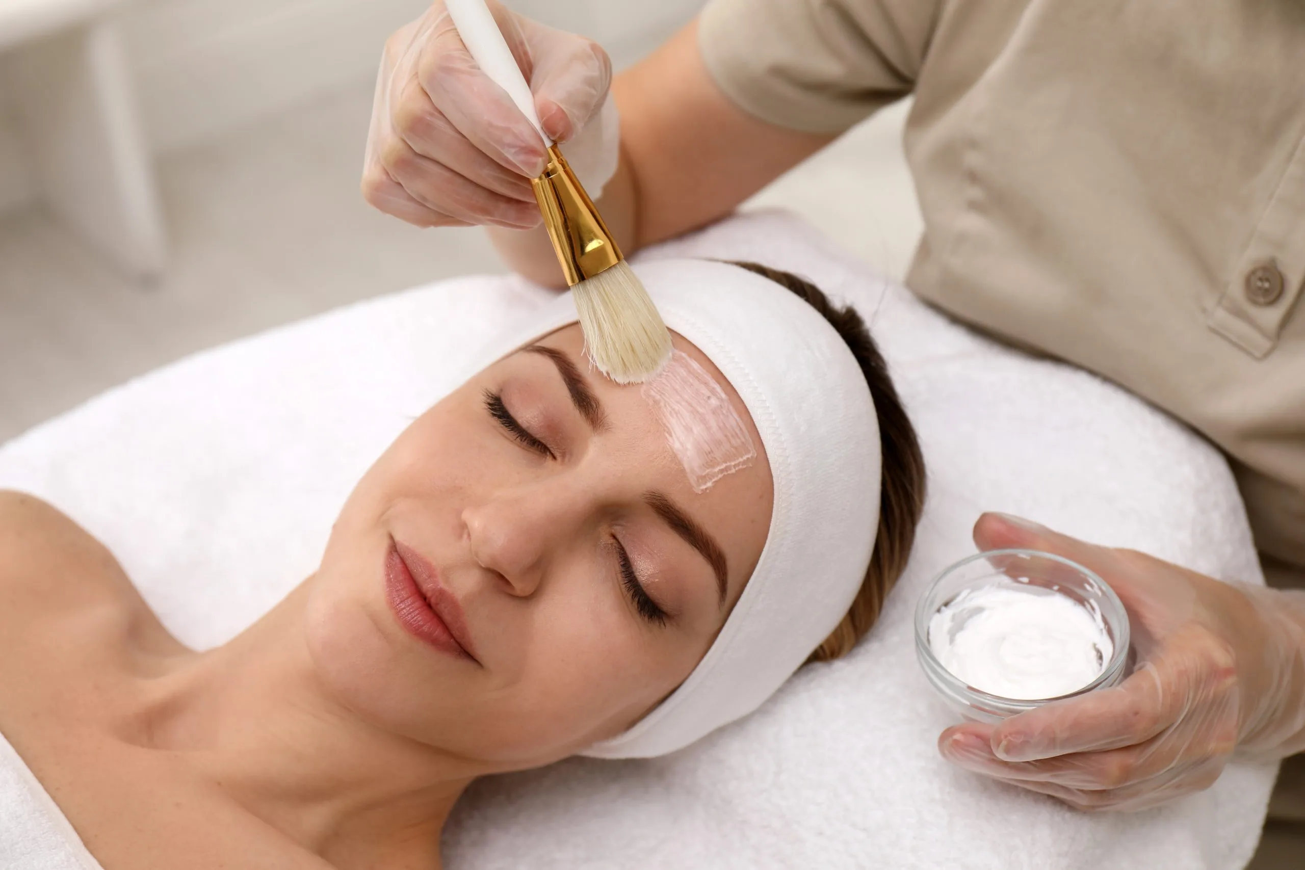 Esthetician applying chemical peel solution to a patient's face with a brush during a facial treatment