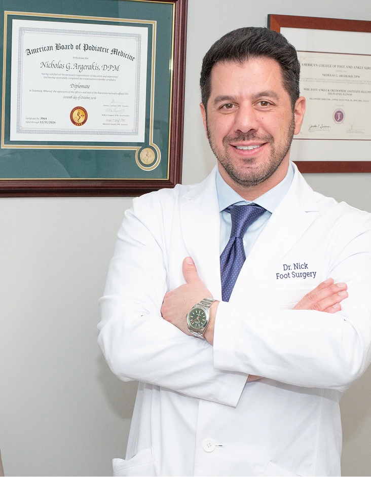 Dr. Nick, podiatric surgeon, smiling with arms crossed in white coat in front of framed certifications