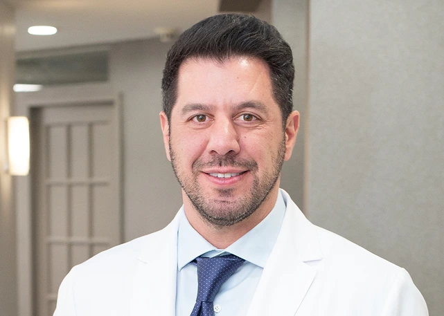Male podiatric surgeon smiling in white coat and blue tie in clinic hallway