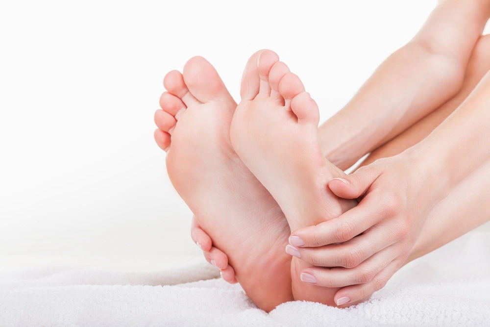 Hands massaging the soles of two bare feet on white towel