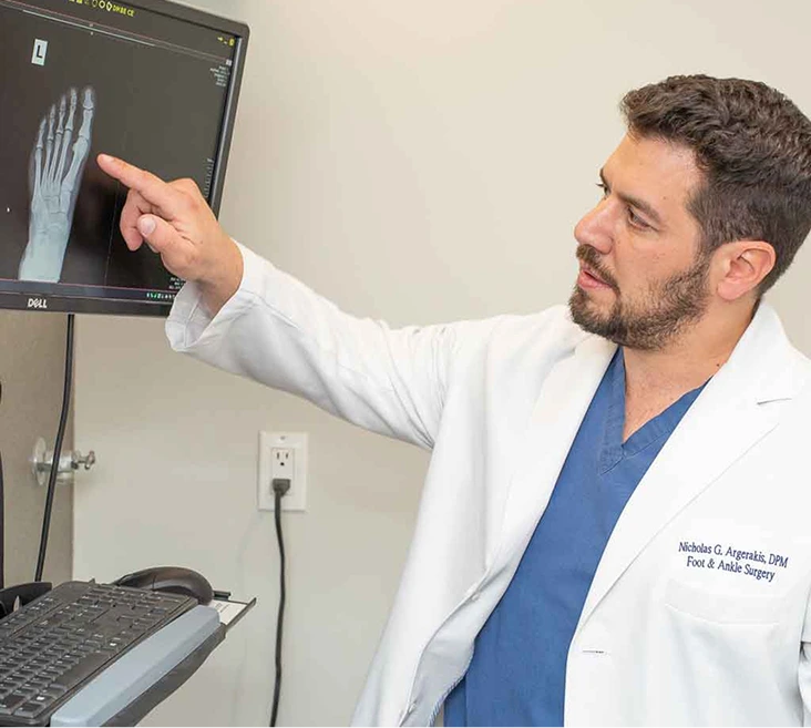 Podiatrist reviewing foot x-ray on monitor with patient in clinical examination room