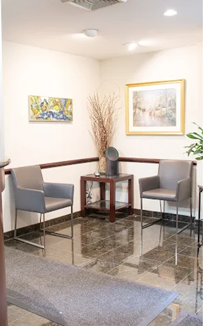 Modern podiatry clinic waiting room with gray chairs, wood table, framed artwork, and potted plant