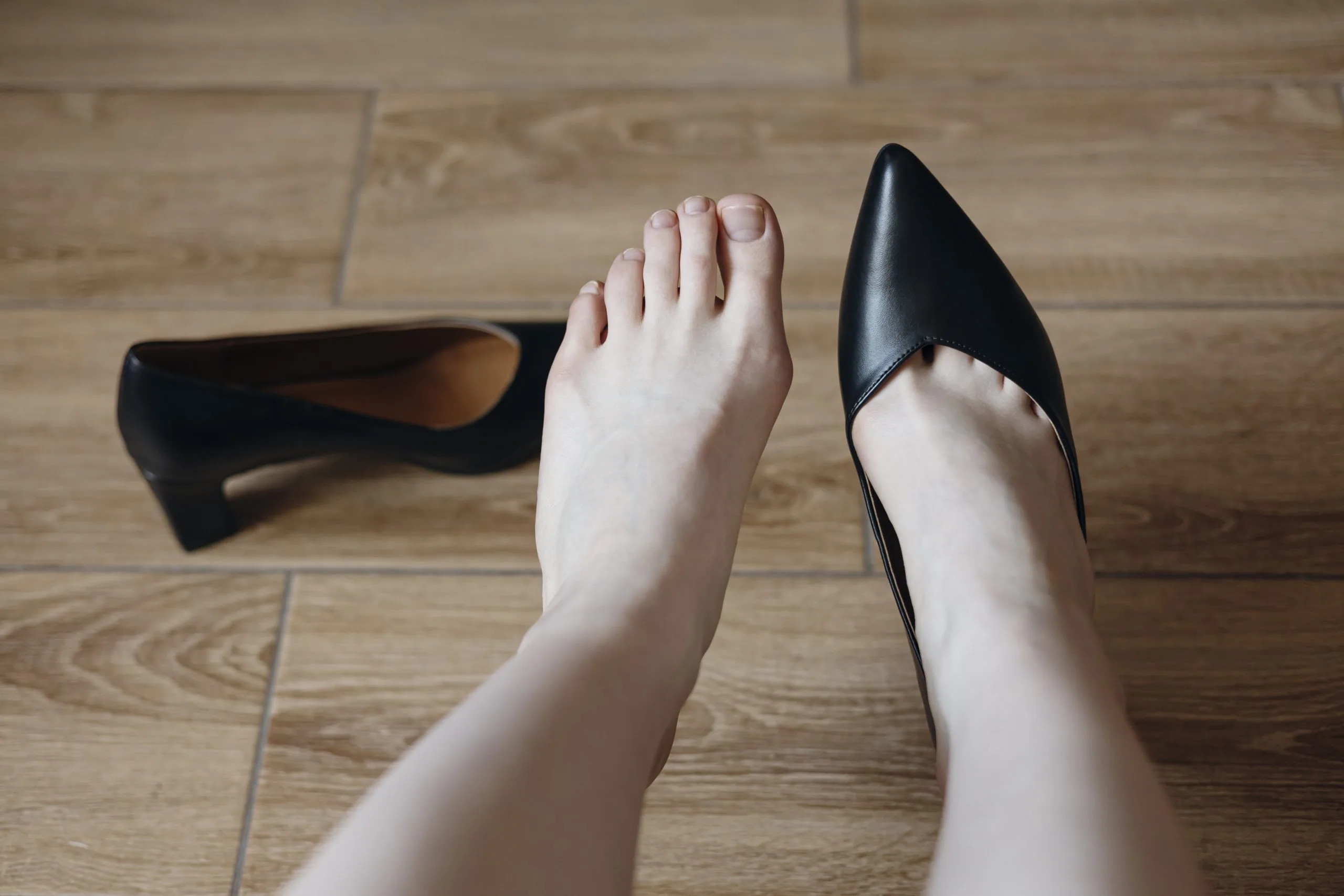 Person wearing black heels experiencing foot pain while standing on wooden floor