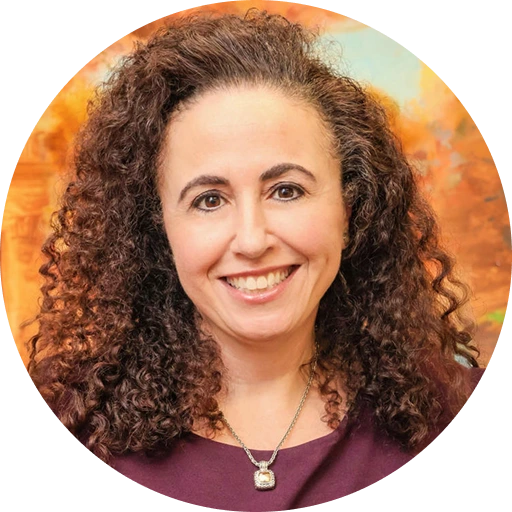 Woman with curly brown hair wearing maroon top and pendant necklace, smiling at camera against orange background