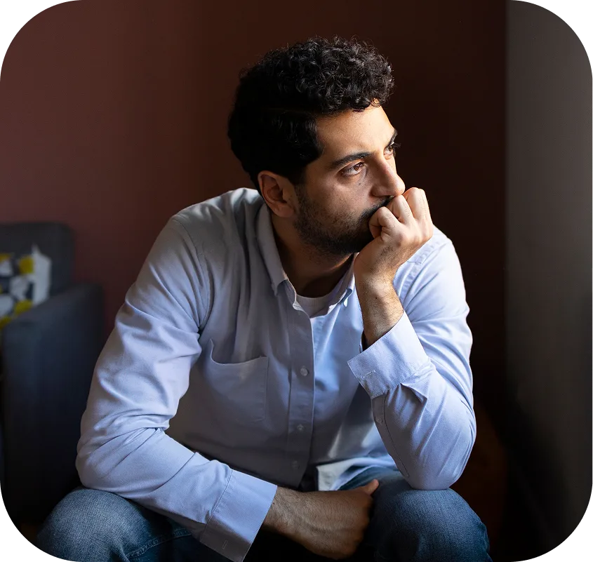 Man in light blue shirt with hand to face, appearing worried or stressed against a dark background